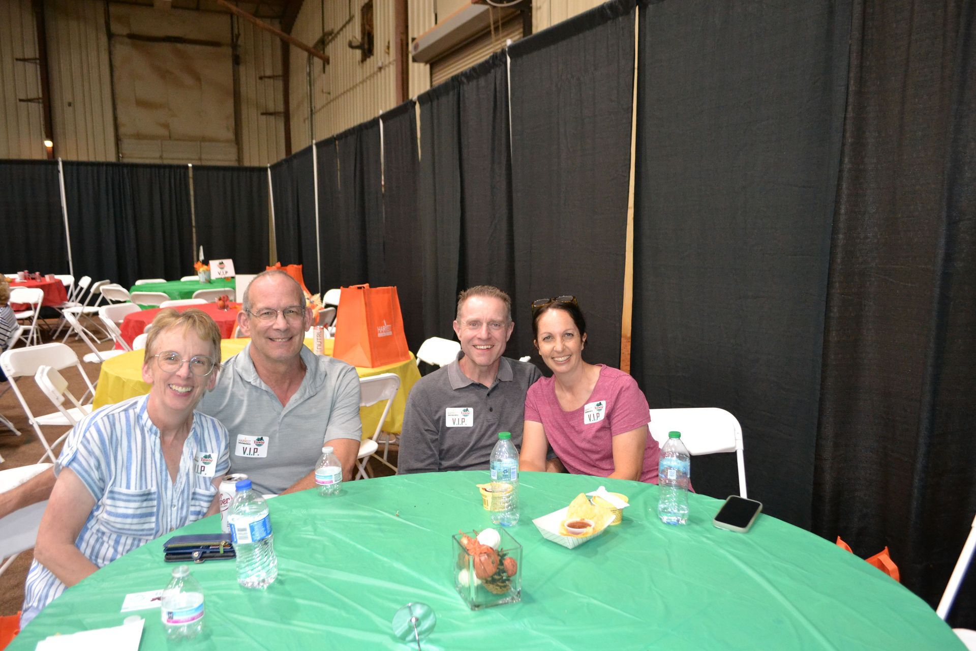 Four people seated at a green table in a banquet hall, smiling toward the camera.