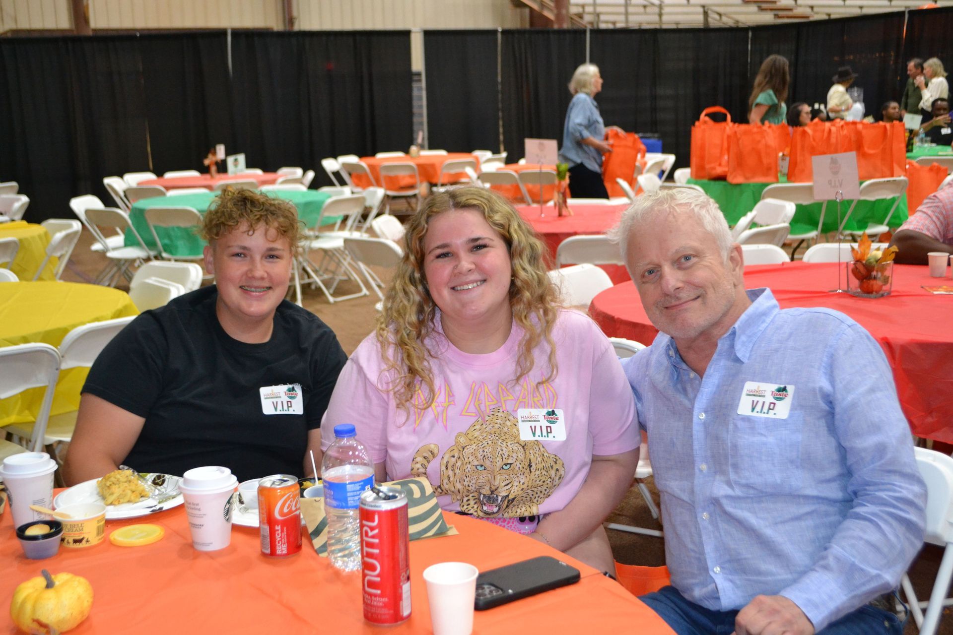 Three people seated at an orange table in a banquet hall, smiling with drinks and plates in front of them.