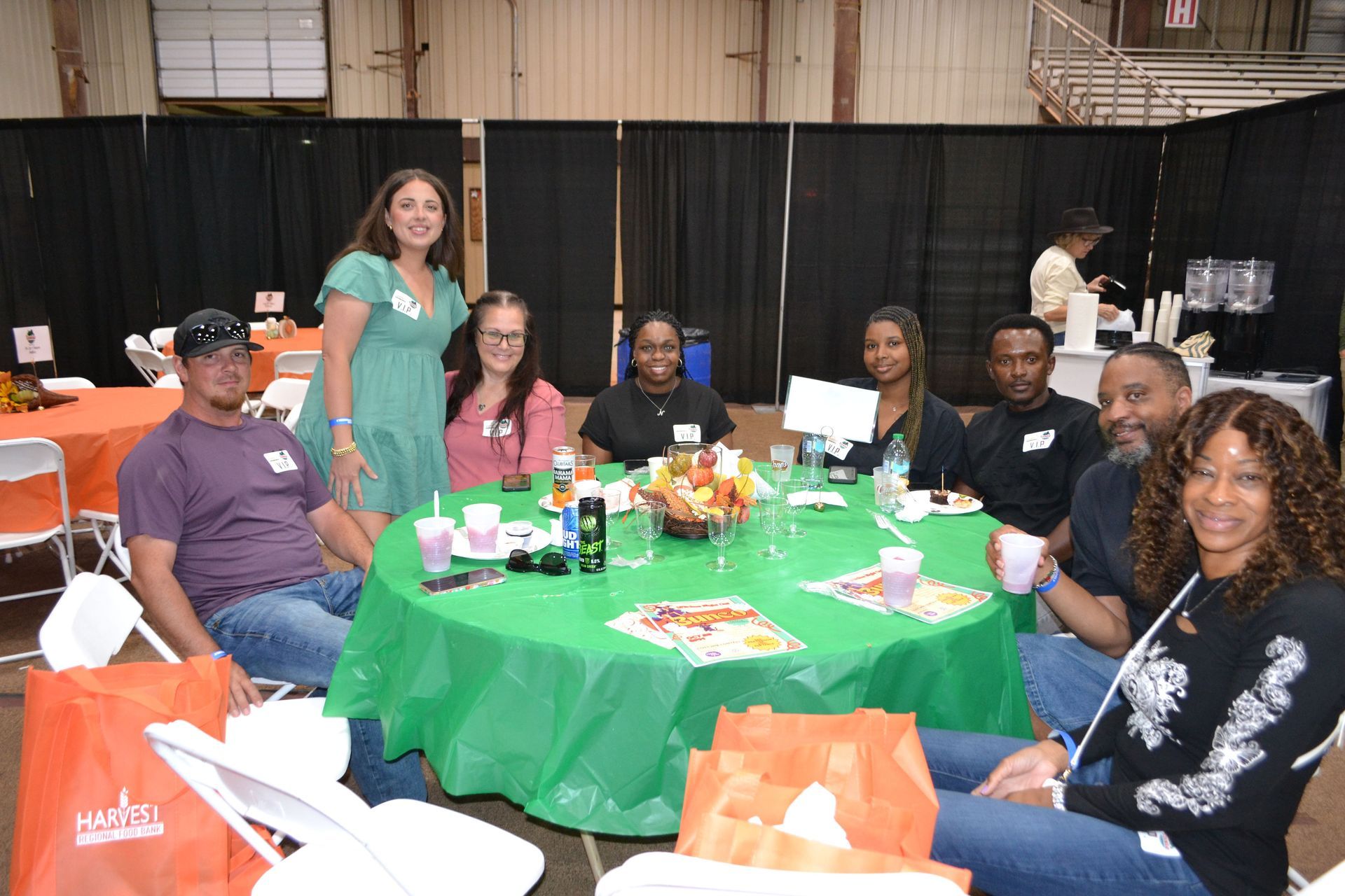 People seated around a green-covered table at an indoor gathering, smiling and posing for a photo.