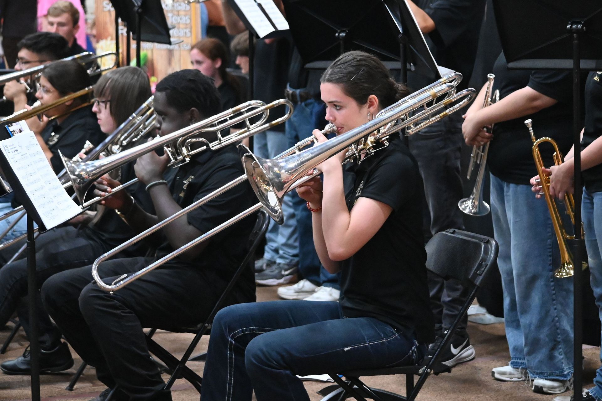 Musicians seated and playing trombones in an outdoor ensemble performance
