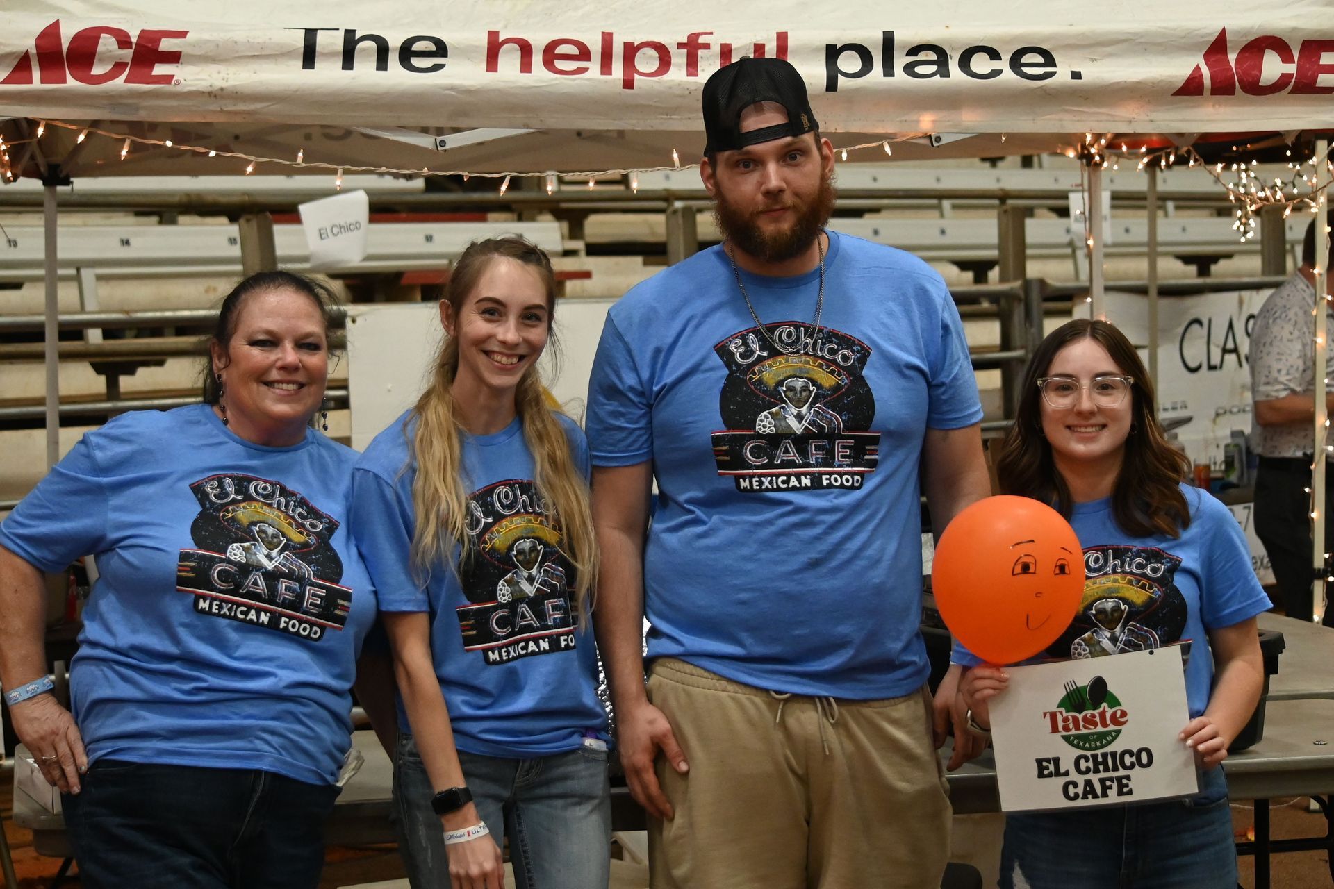Four people in blue shirts stand in a hardware store, holding a sign and orange balloon.