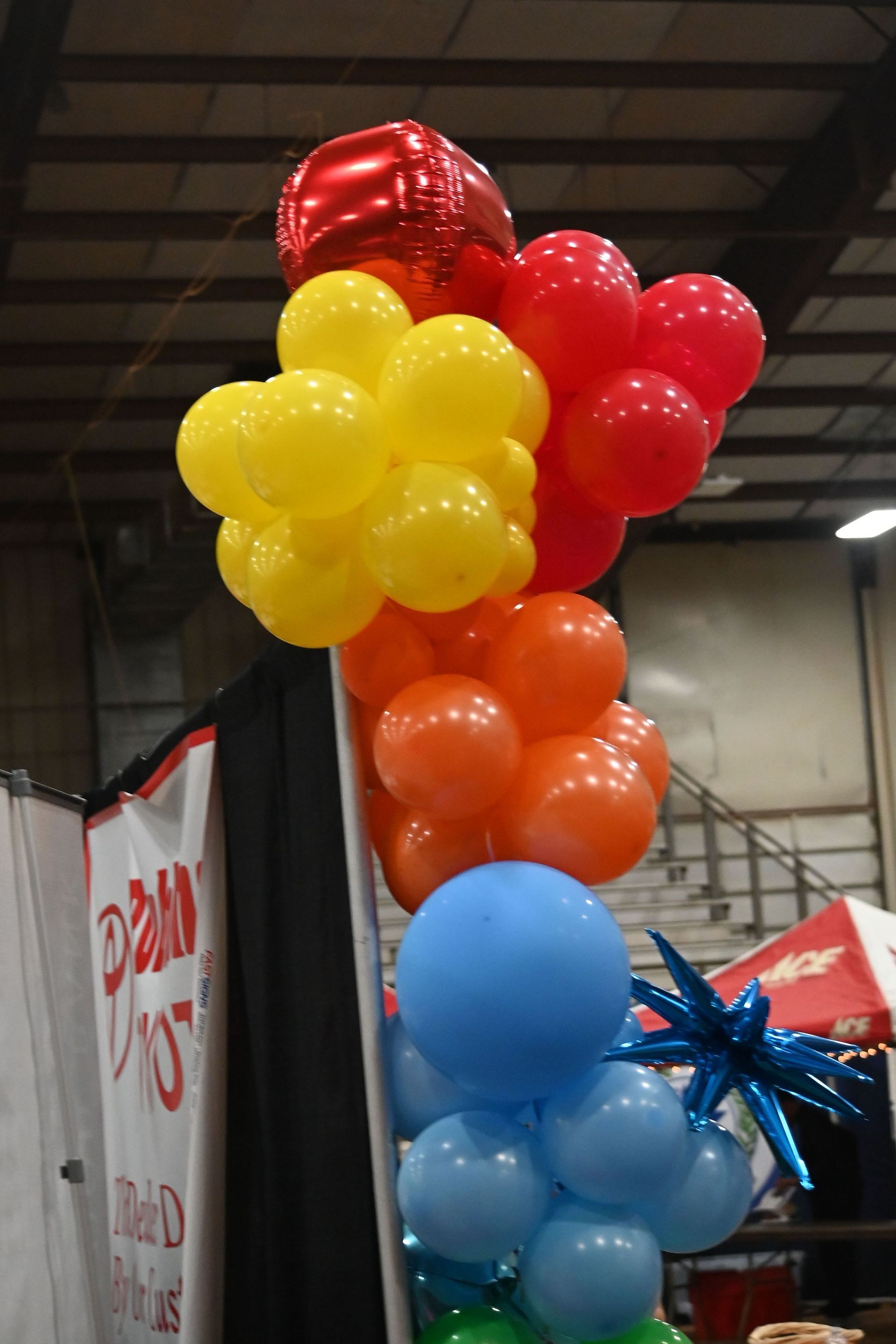 Colorful balloon bouquet in red, yellow, orange, and blue at an indoor event booth