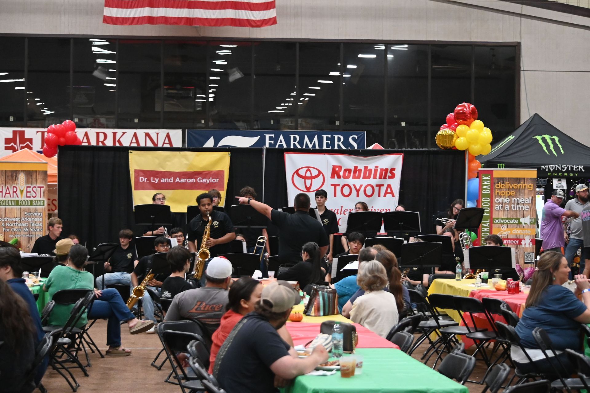 Outdoor fundraiser with seated audience, live band, and sponsor banners at a storefront stage