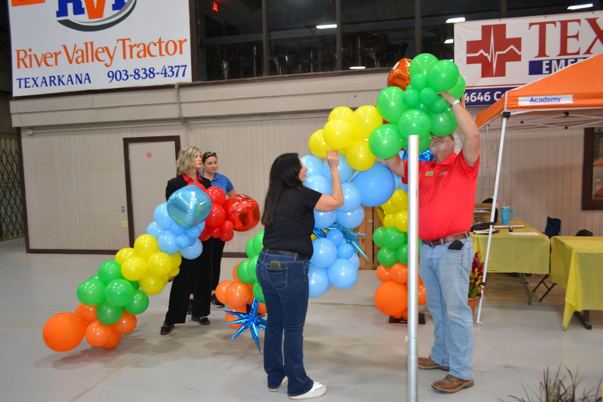 People arranging colorful balloon arches at an indoor event booth