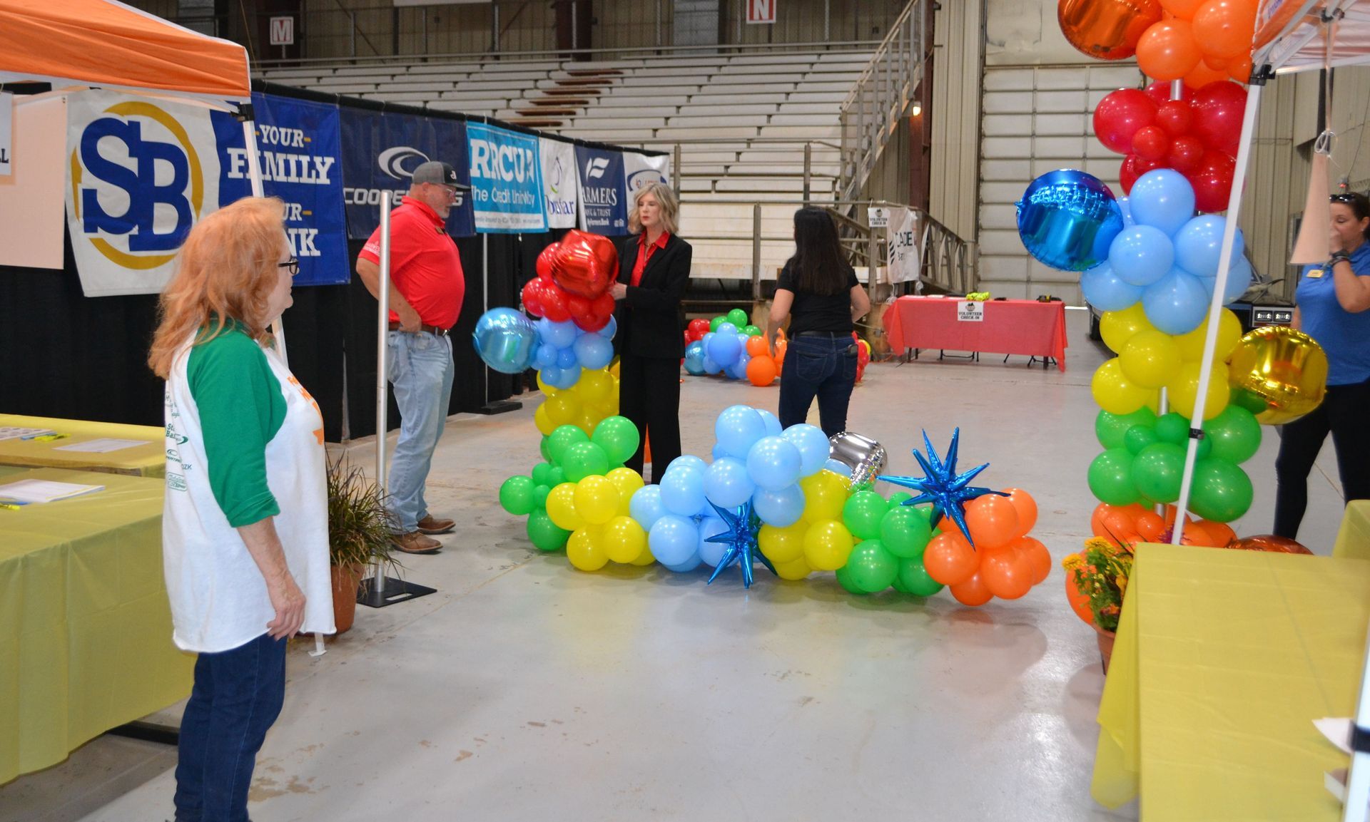 Balloon arch and clusters at an indoor event booth with people standing nearby