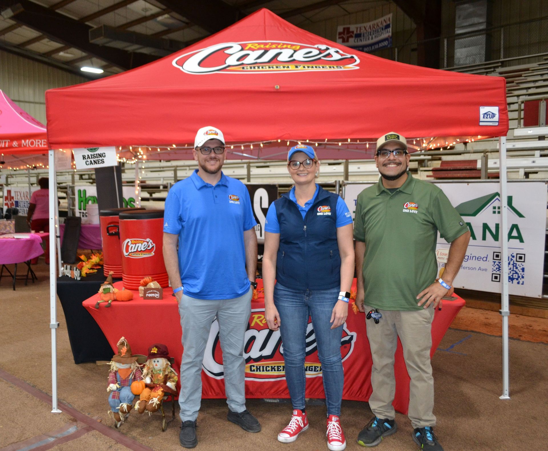 Three people stand at a Canes tent at an indoor event, smiling beside a display table.