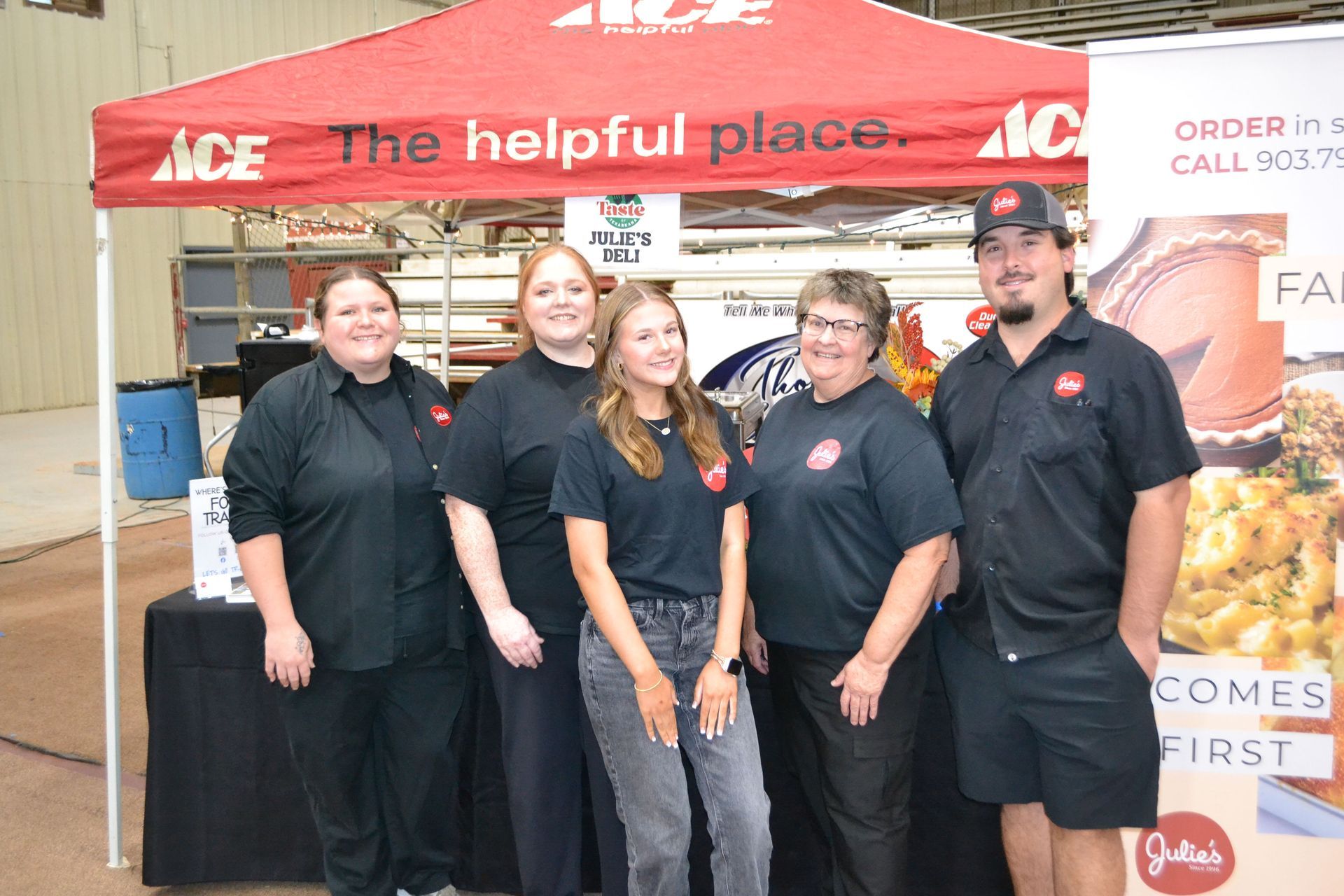 Five people in black shirts stand at an Ace Hardware booth under a red canopy.