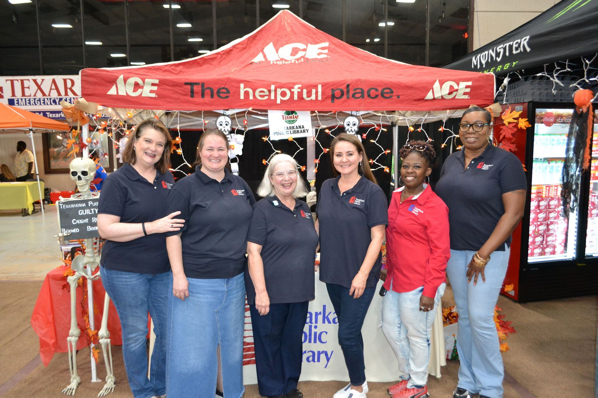 Six people pose inside an ACE Hardware store beneath a red “ACE” canopy.