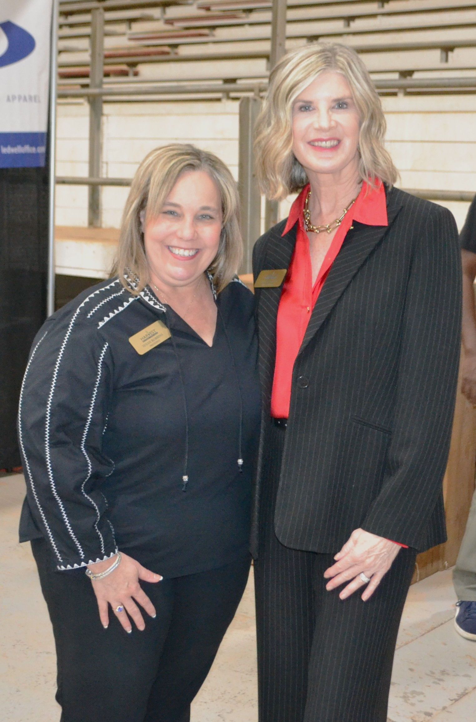 Two women standing indoors, smiling in business attire near a striped wall.