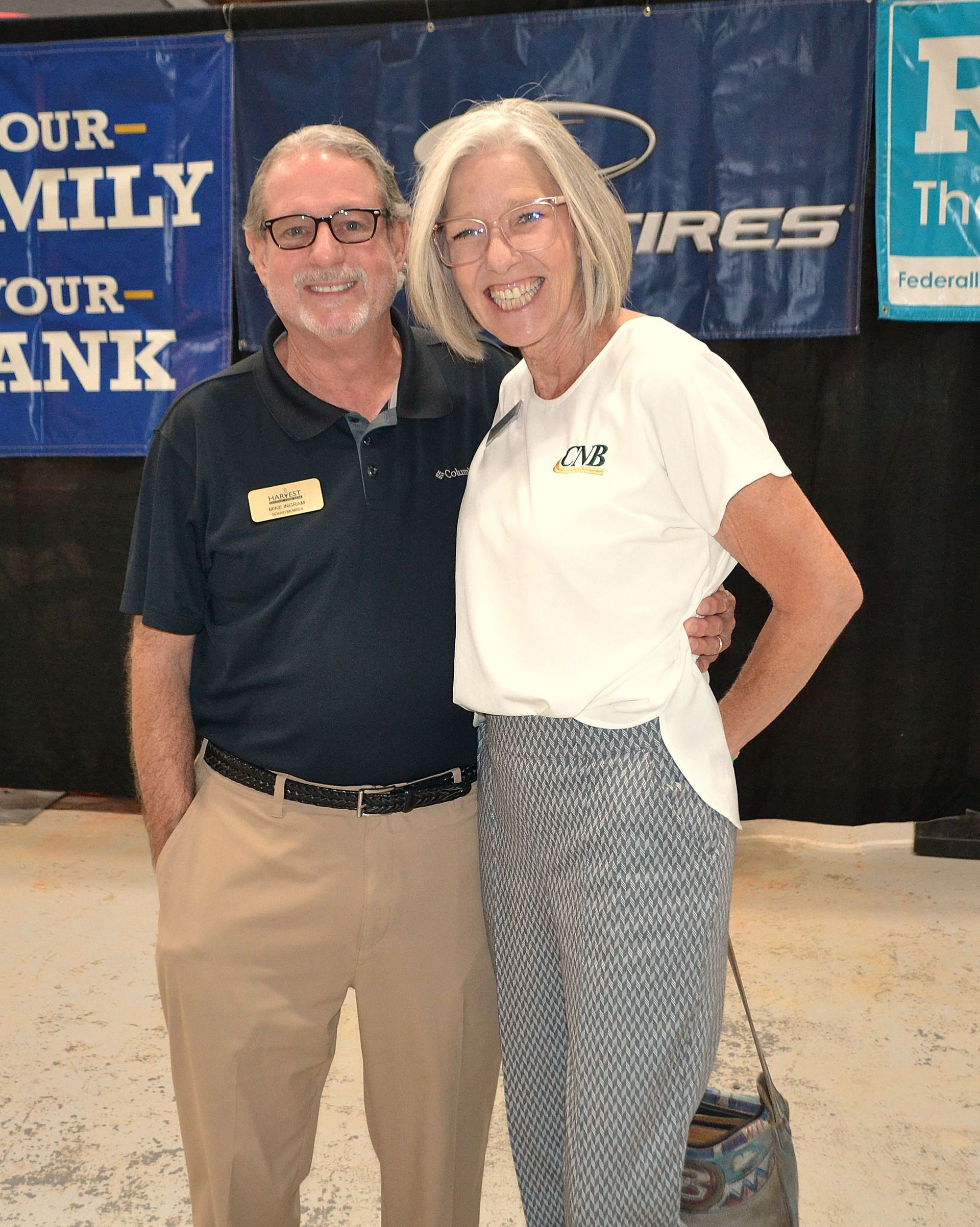 Smiling couple posing at an event booth, with blue banners in the background.