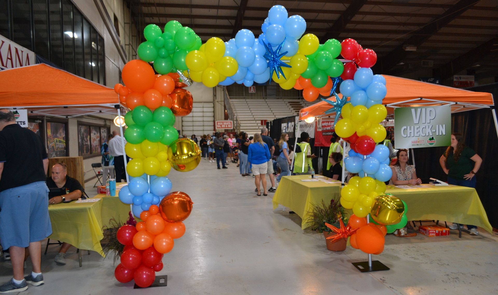Balloon arch at an indoor market with vendor tables and colorful display balloons on both sides