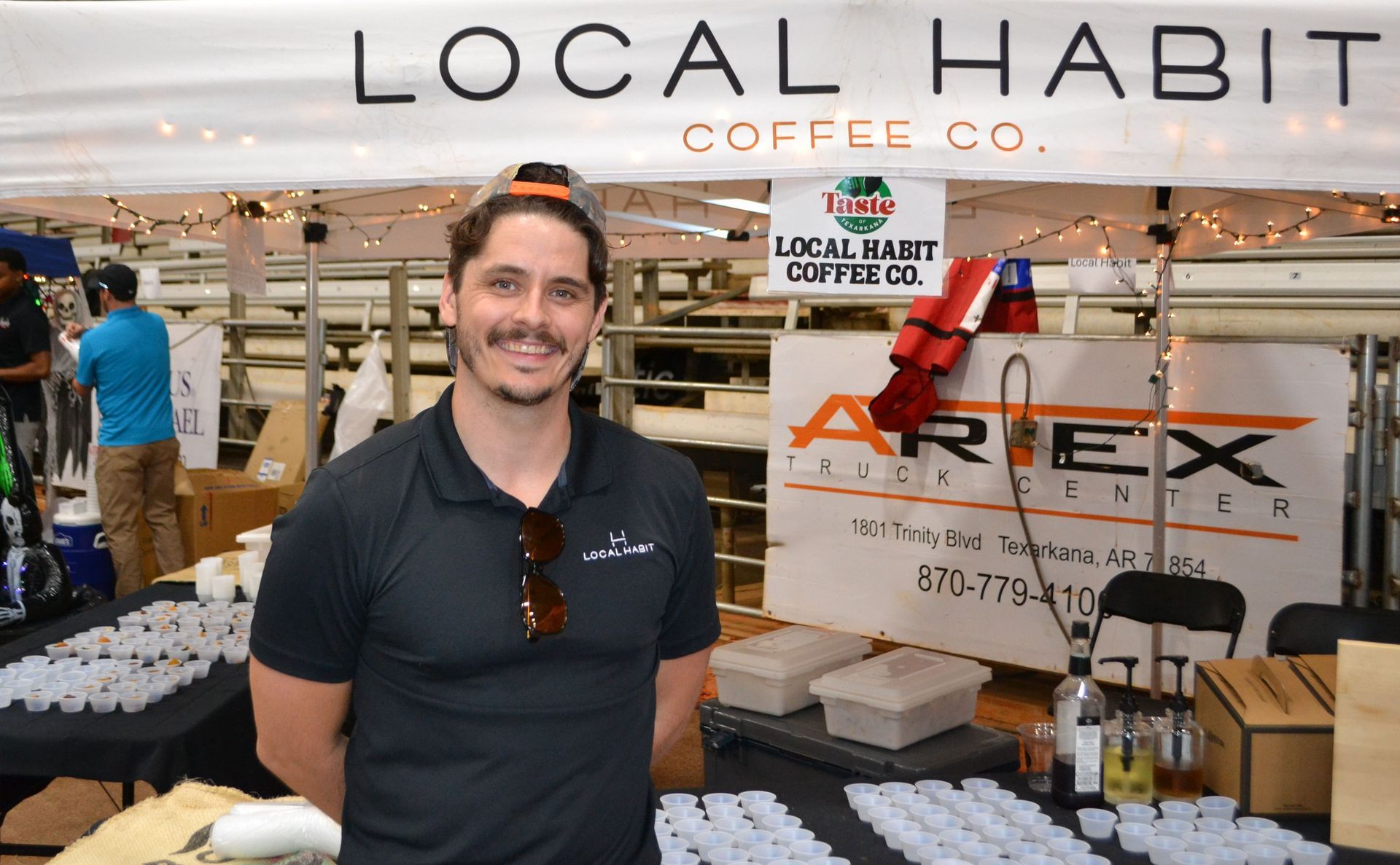 Man standing at a Local Habit Coffee Co. booth with bags and a sign in the background