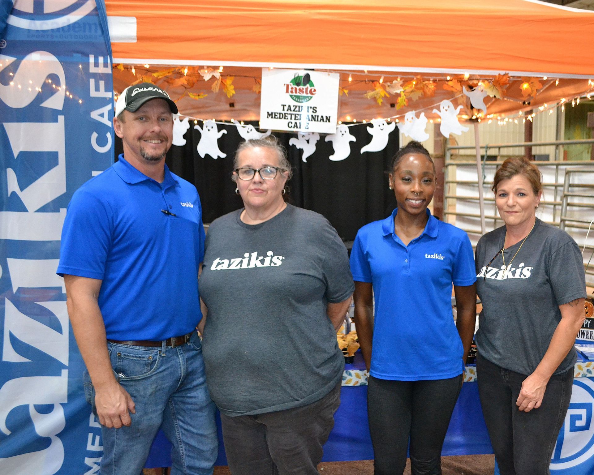 Four people in blue and gray work shirts standing at a café booth display.