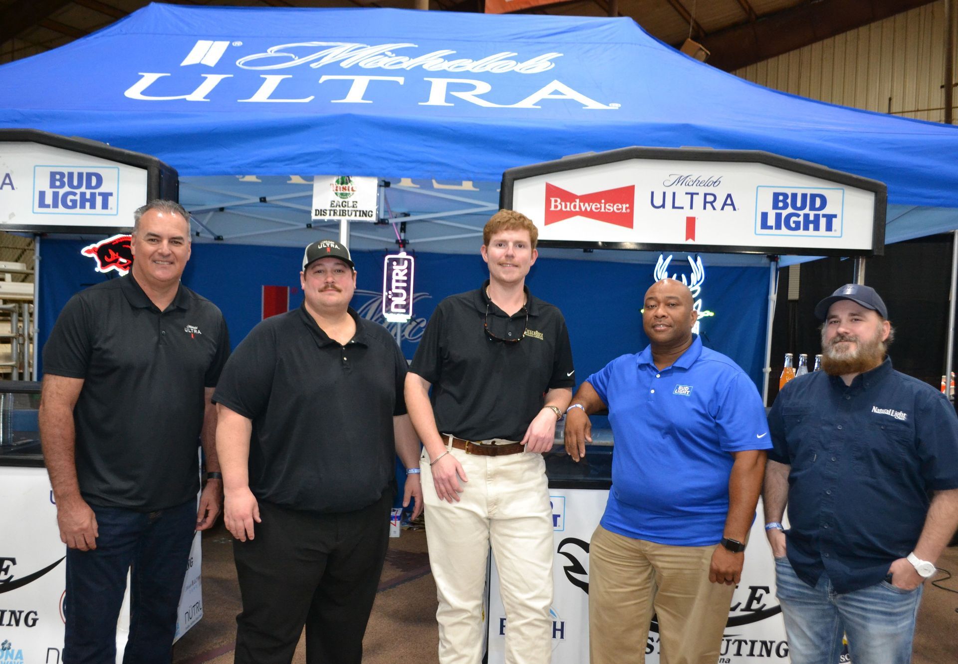 Five men posing under a blue Bud Light Ultra tent at an event booth