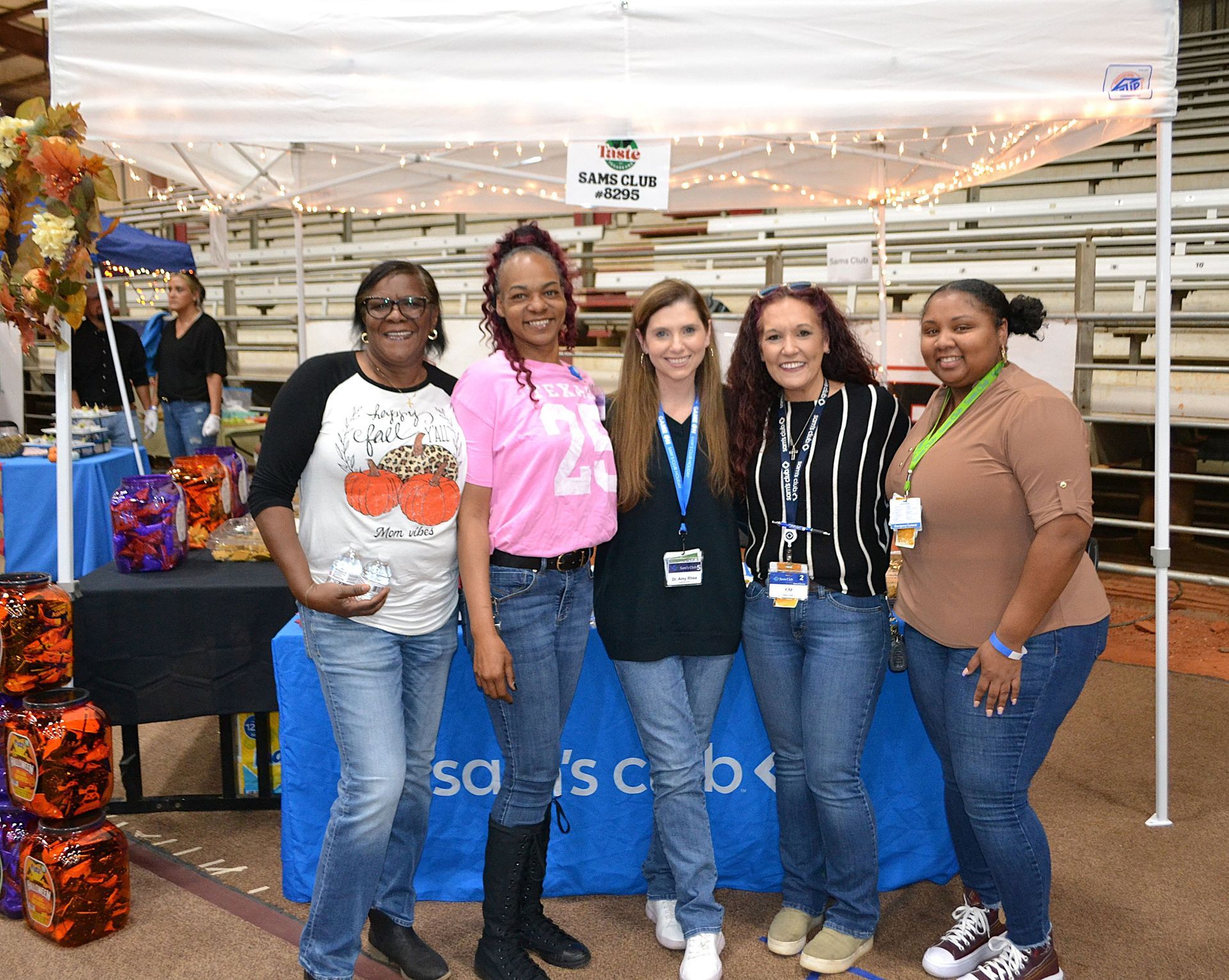 Five people stand smiling in a store aisle, wearing lanyards, beside a blue display table.