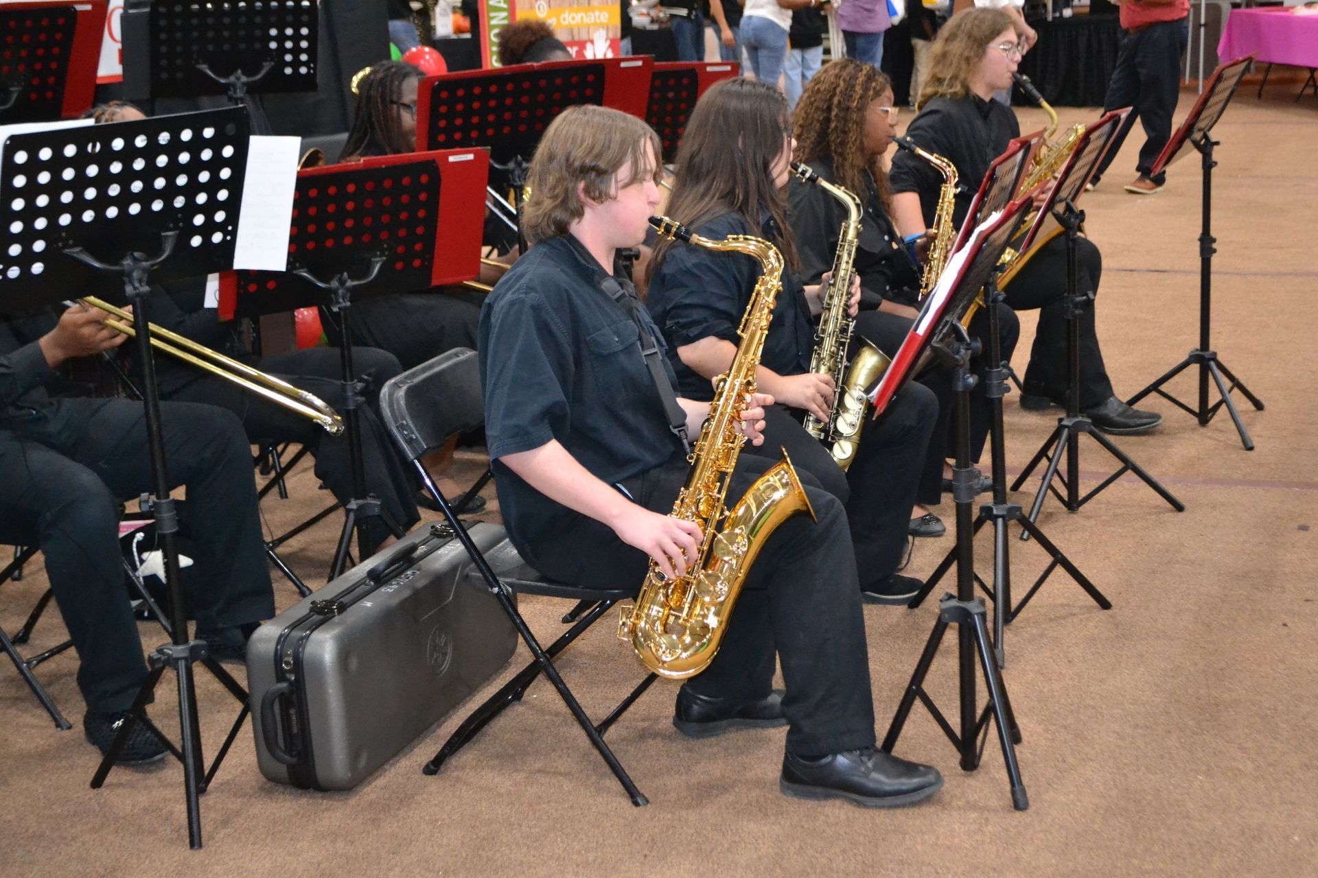 Students playing saxophones in a school band rehearsal with music stands and chairs