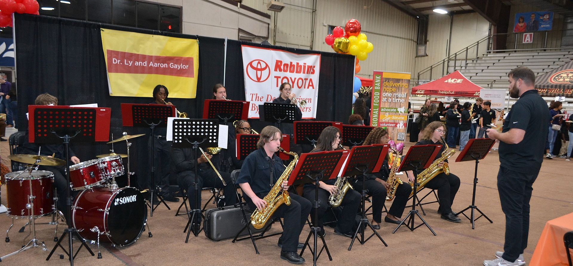 School band performing indoors with brass and percussion instruments on a stage-like setup