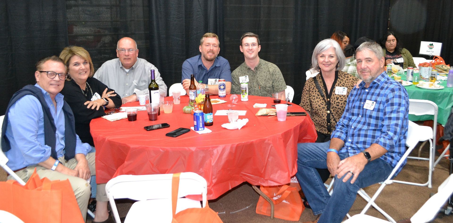 People seated around a red-clothed table at a social gathering, smiling indoors.