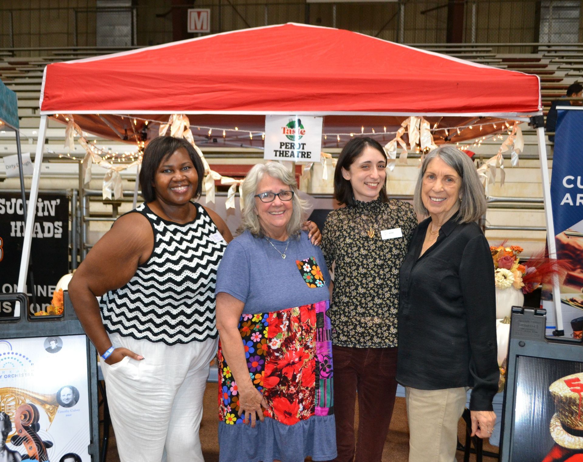Four women posing in front of a red canopy at an indoor market booth