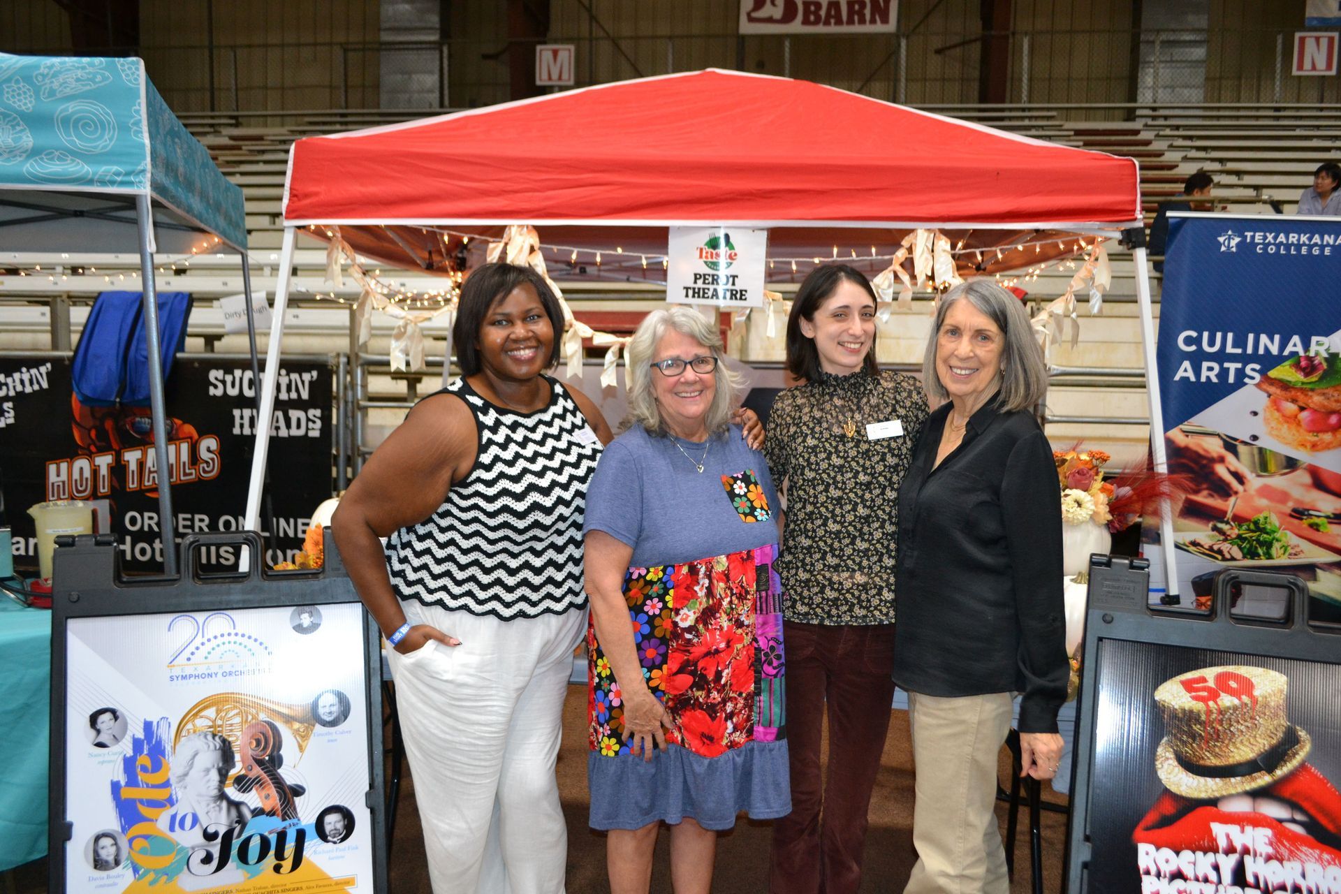 Four people pose under a red canopy at a fair booth with colorful promotional signs.