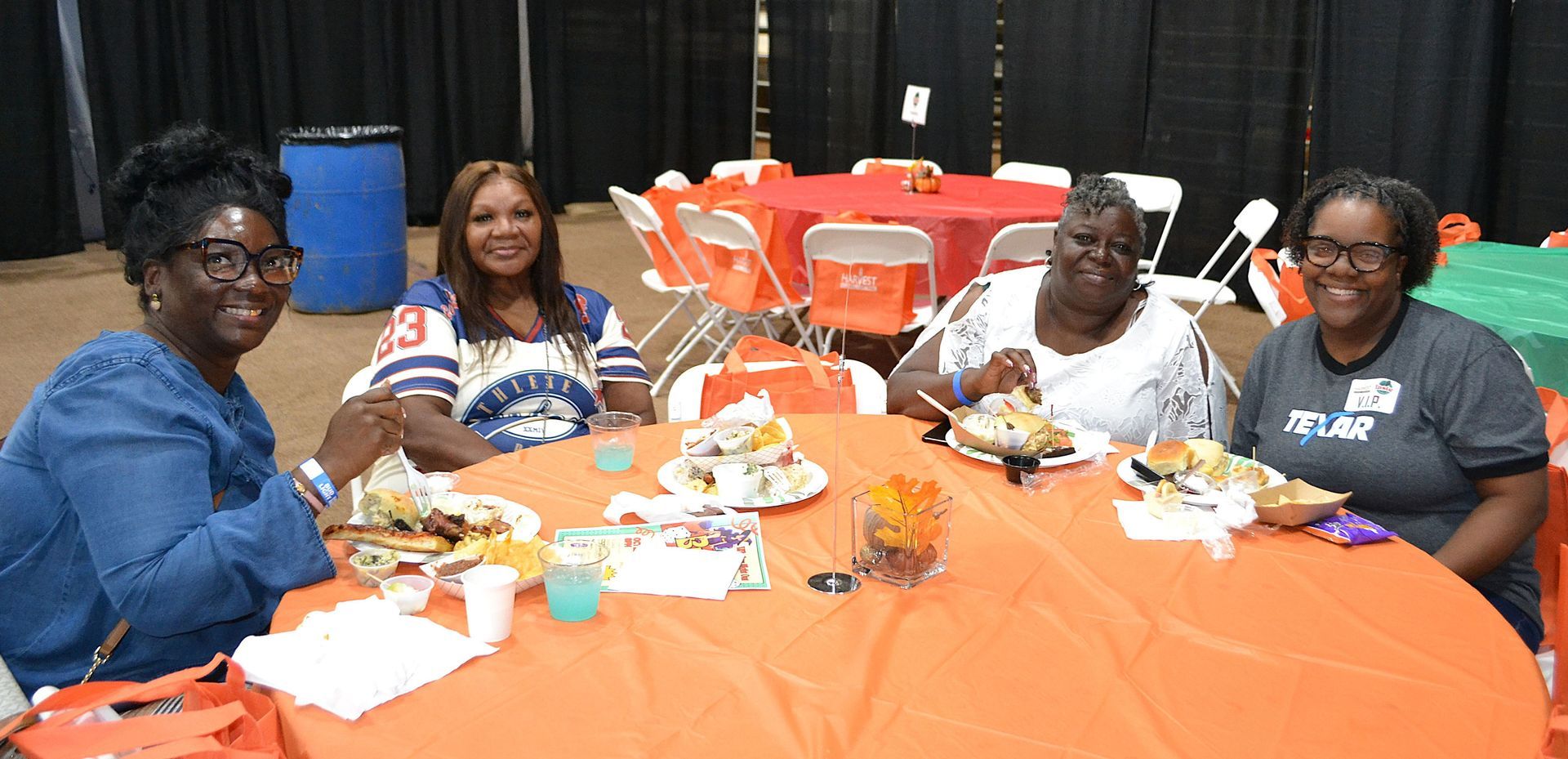 People seated at a round table with orange tablecloths in a banquet hall, smiling and eating