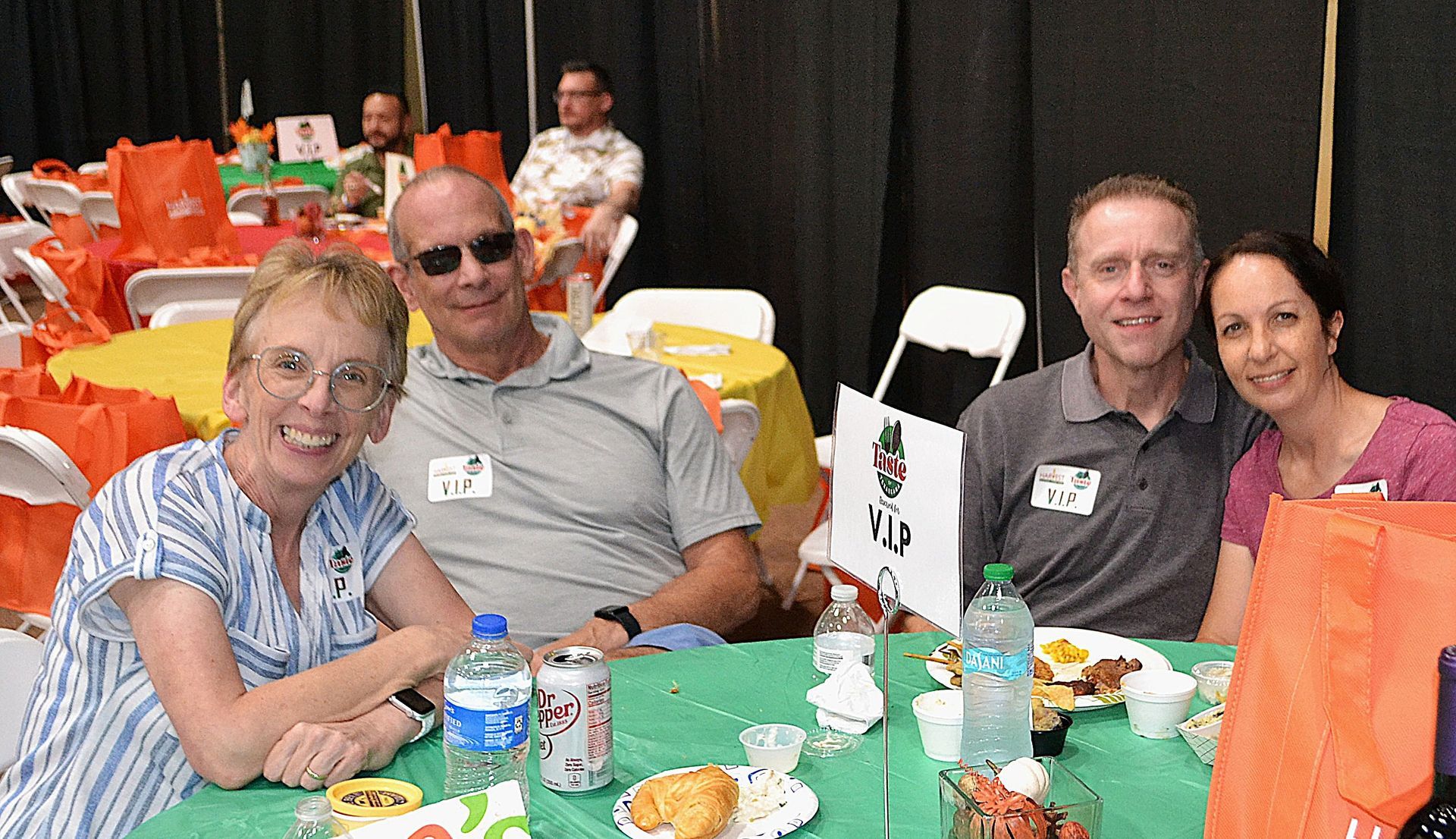 People sitting at a banquet table with drinks and snacks, smiling at an indoor event.