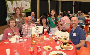 Six people seated at a red table at a lively indoor event, smiling toward the camera.