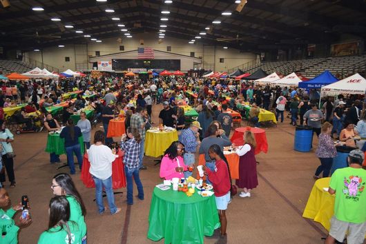 Crowded indoor event hall with booths, tables, and people mingling under bright lights