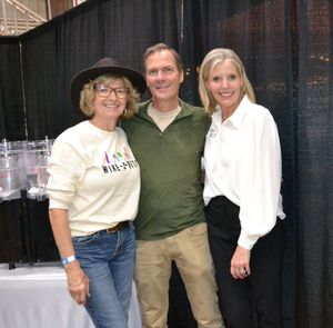 Three people posing together at an indoor event, smiling in front of black curtains.