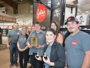 Group posing indoors with plaques and trophies in front of a red Grubbs sign.