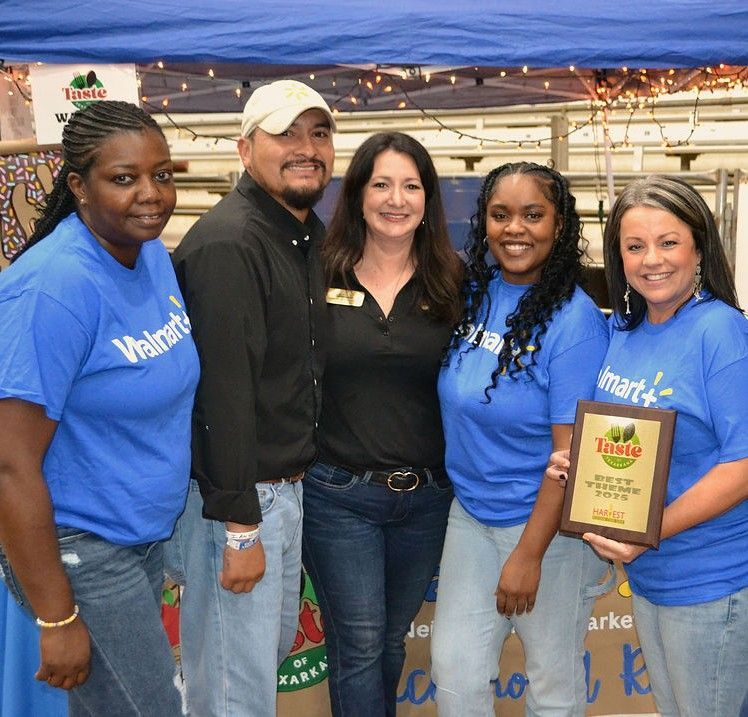 Five people at an event booth, smiling and holding an award plaque under a blue tent.