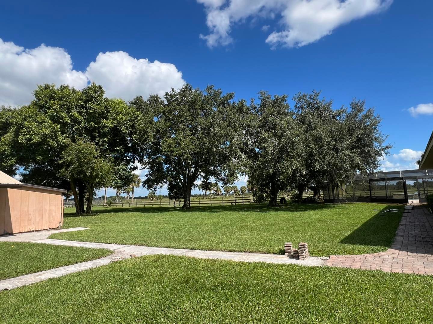 Sunny grassy yard with trees, gravel paths, and a blue sky with clouds