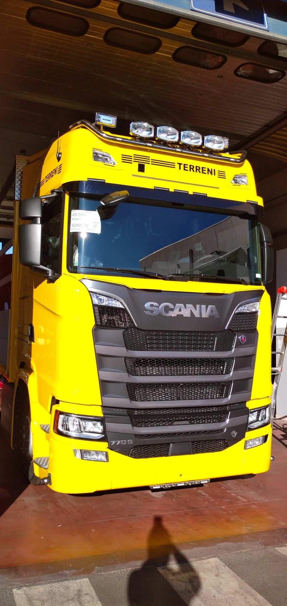 La cabina di un camion Scania di un giallo acceso, con fari supplementari sul tetto, è parcheggiata all'interno su un pavimento rosso.