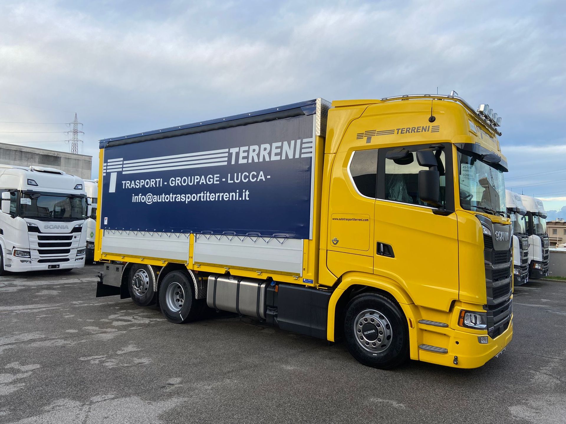 Un camion Scania giallo brillante con un rimorchio telonato blu scuro con la scritta 