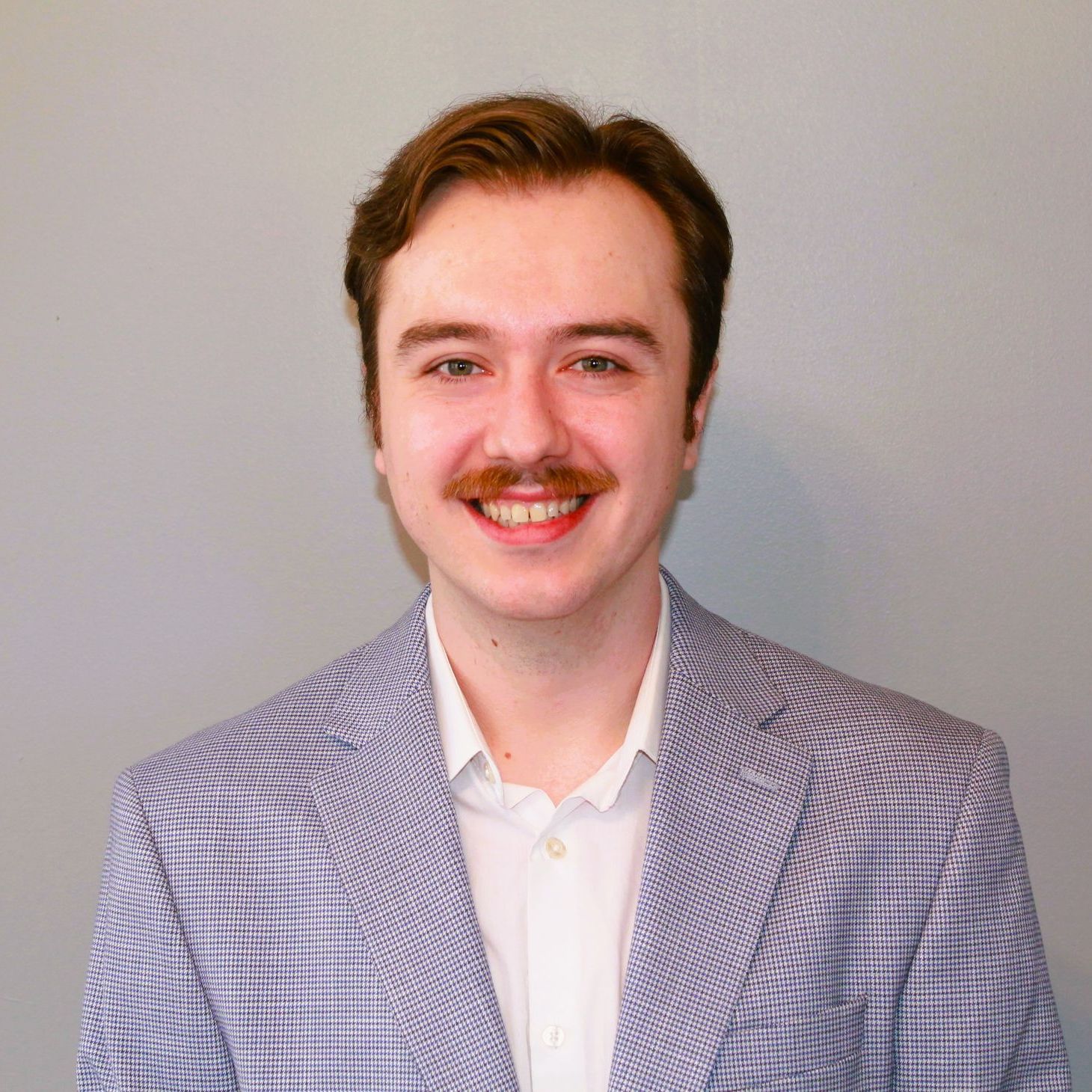 A man with a mustache is wearing a suit and smiling for the camera.