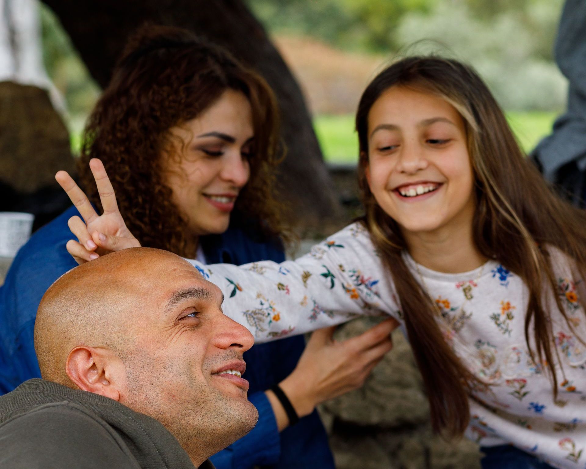 A man and woman are sitting next to a little girl who is giving a peace sign.
