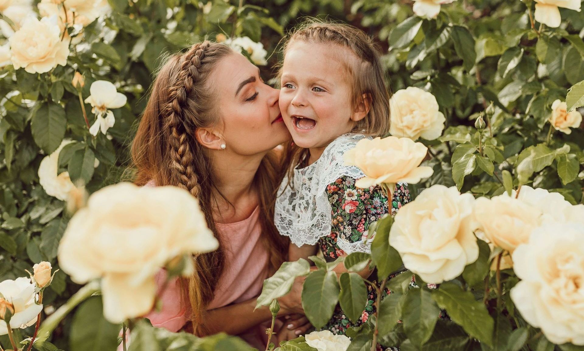 A woman is kissing her daughter on the cheek in a field of flowers.