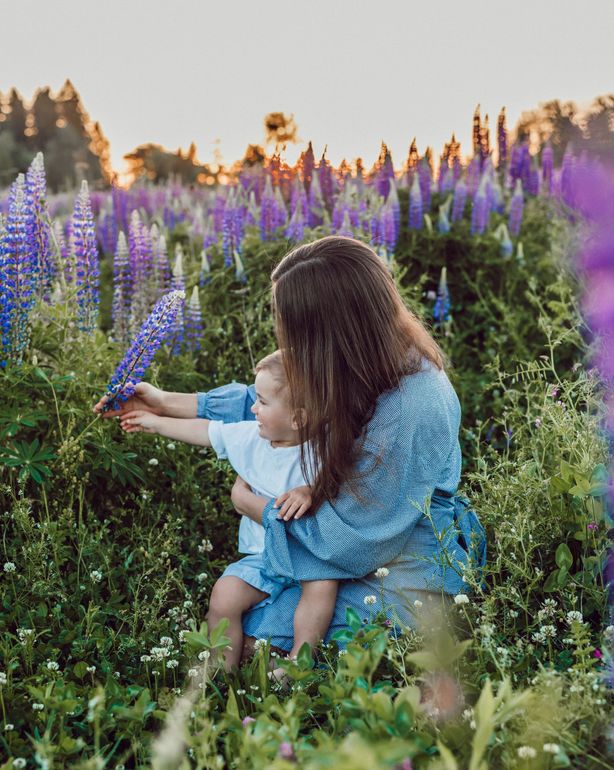 A woman is holding a baby in a field of purple flowers.