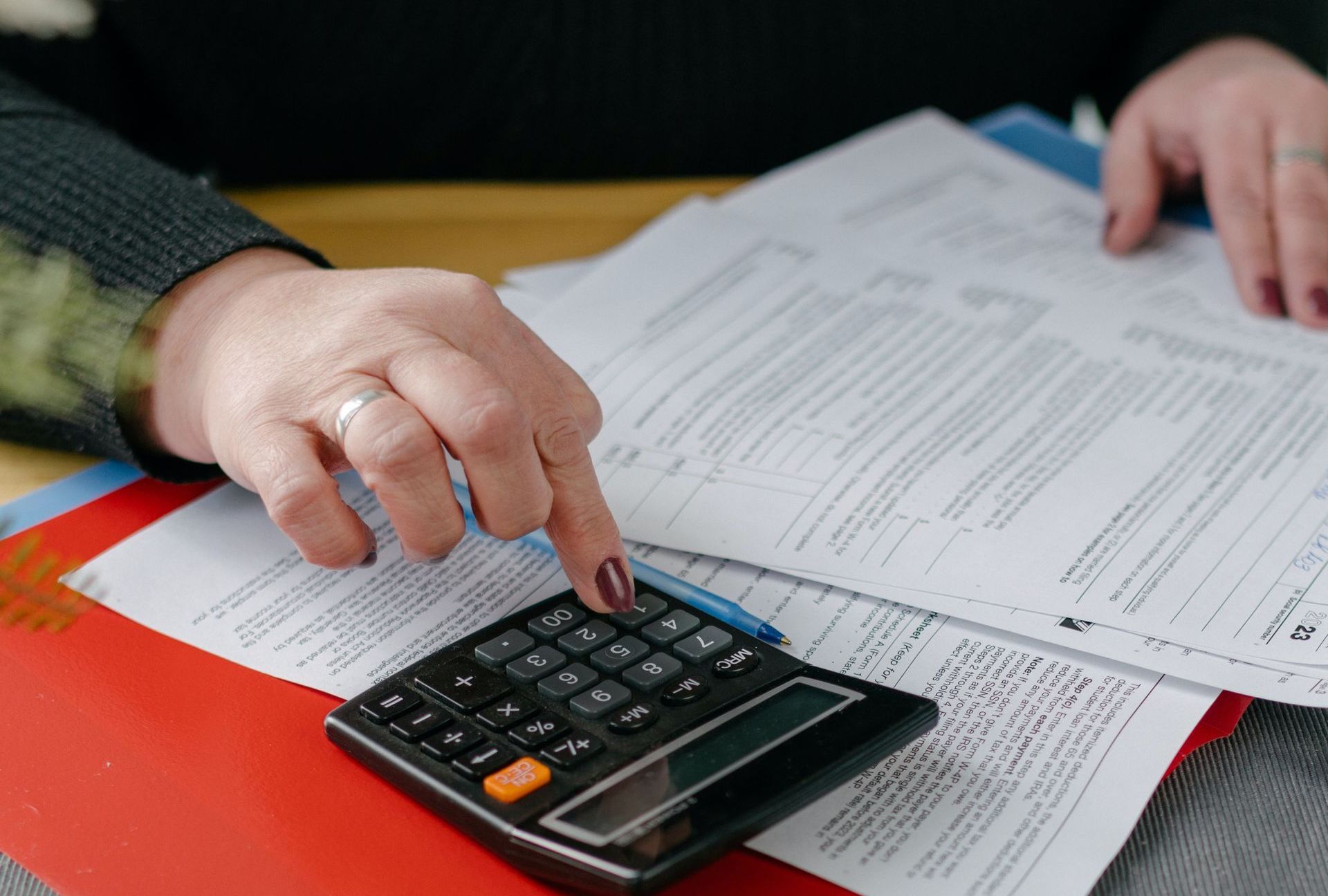 A woman is using a calculator while sitting at a table with papers.