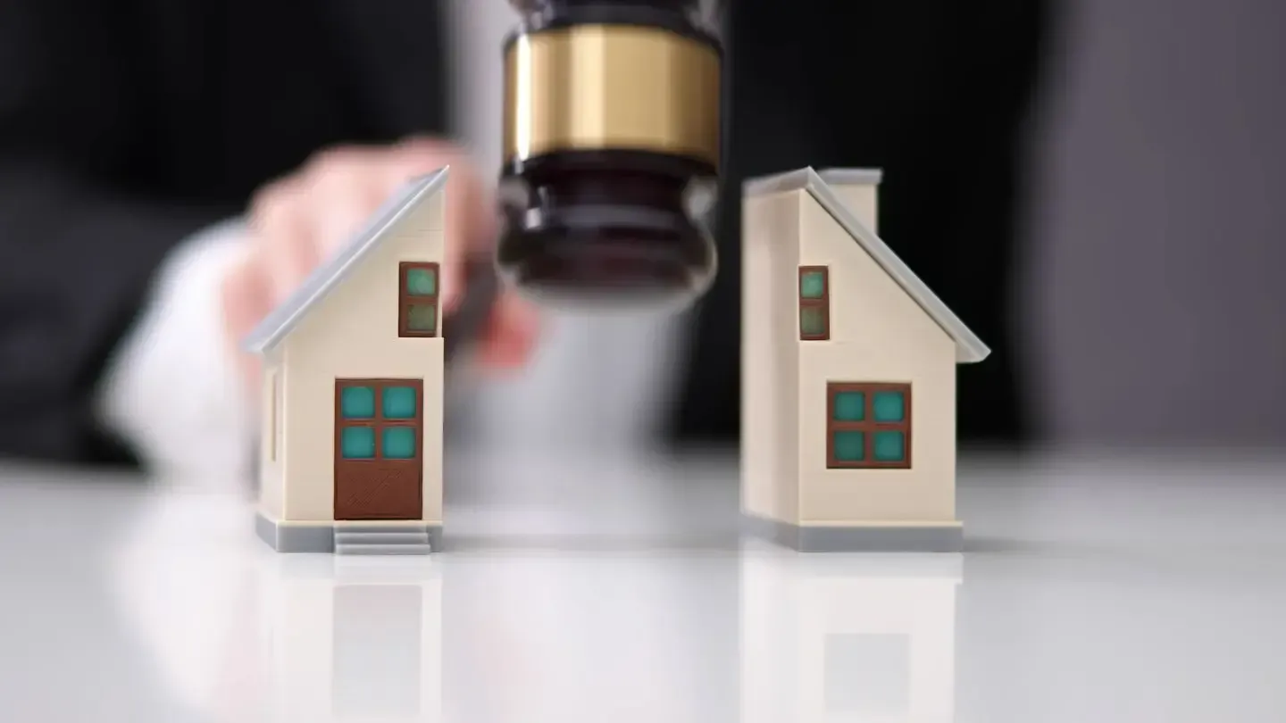 Gavel hitting miniature house split in two halves, symbolizing property division in a divorce.