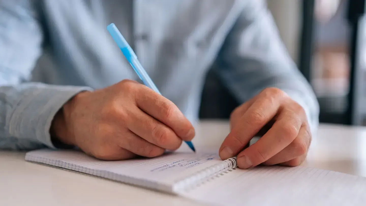 A man is writing his will in a notebook with a pen.