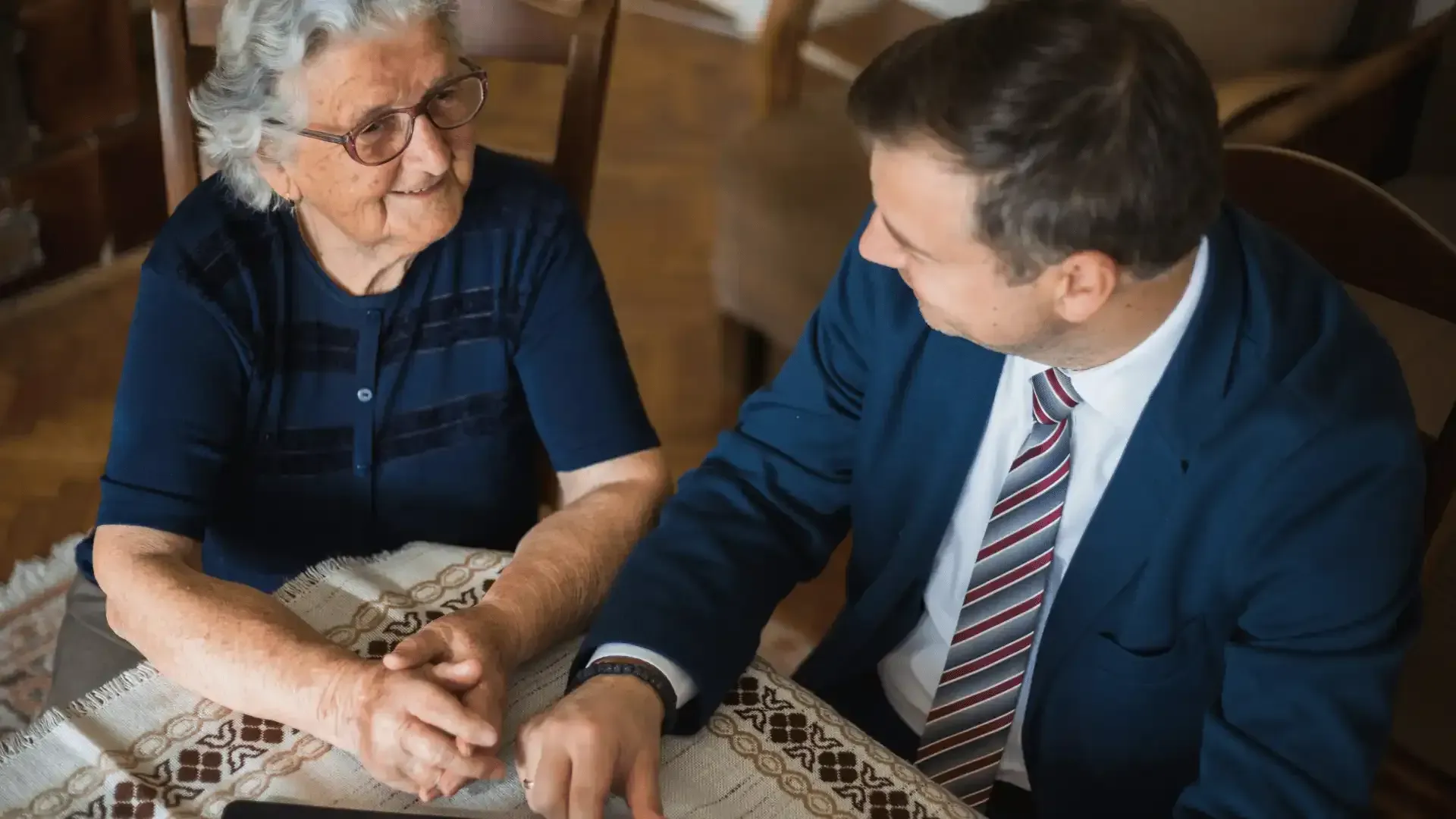 A man and an elderly woman are sitting at a table looking at a tablet.