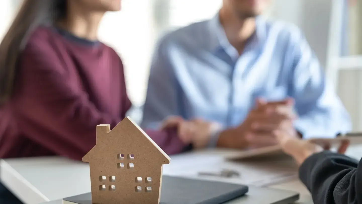 Couple in a meeting with a real estate agent, a house model in the foreground.