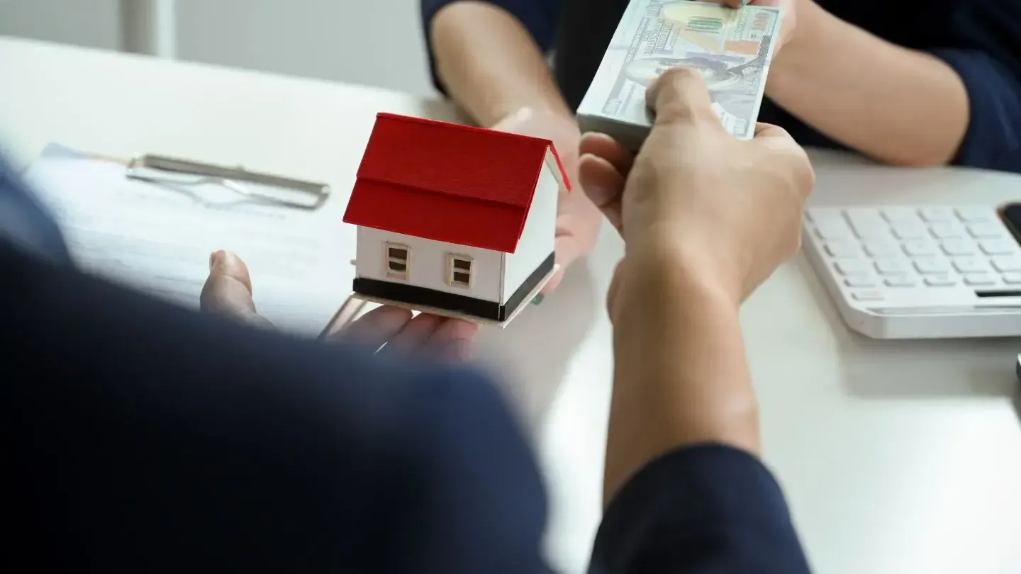 A person is holding a model house and giving money to another person.