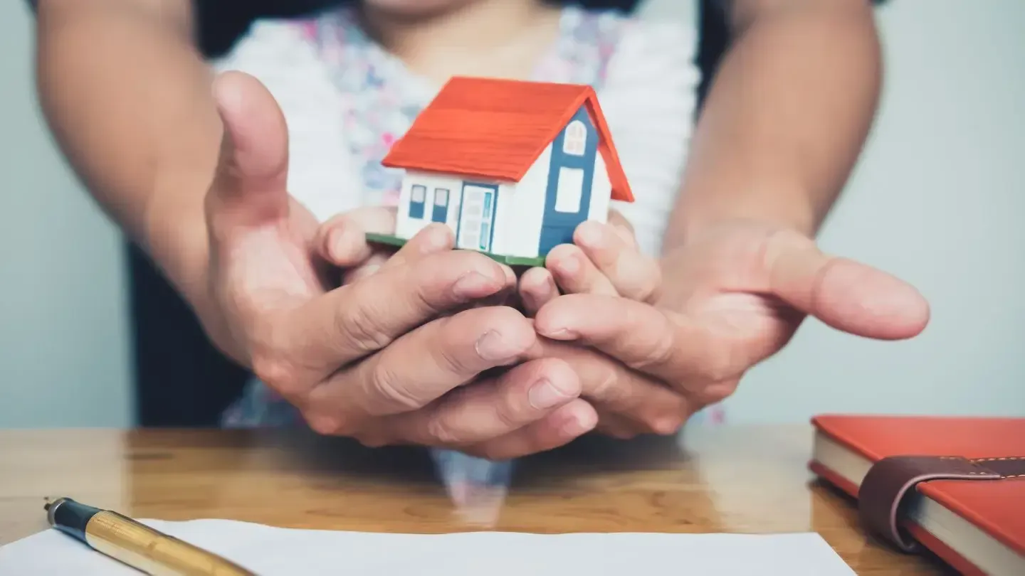 A person is holding a small model house in their hands.