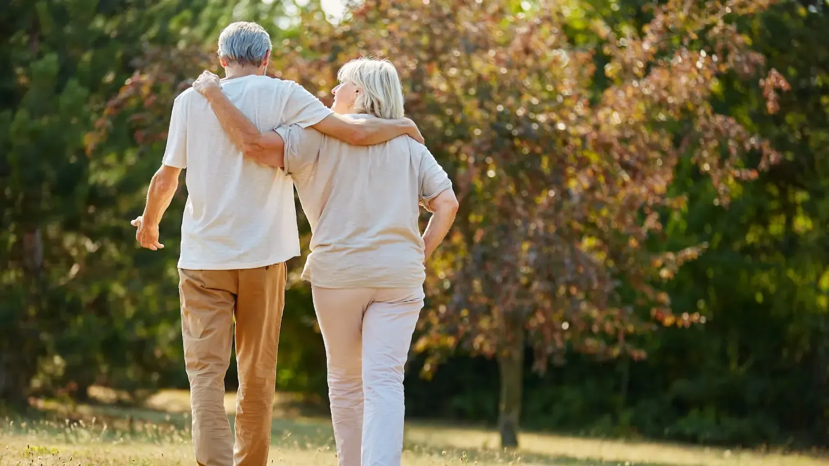 Older couple walking arm in arm in a park, enjoying a sunny day.