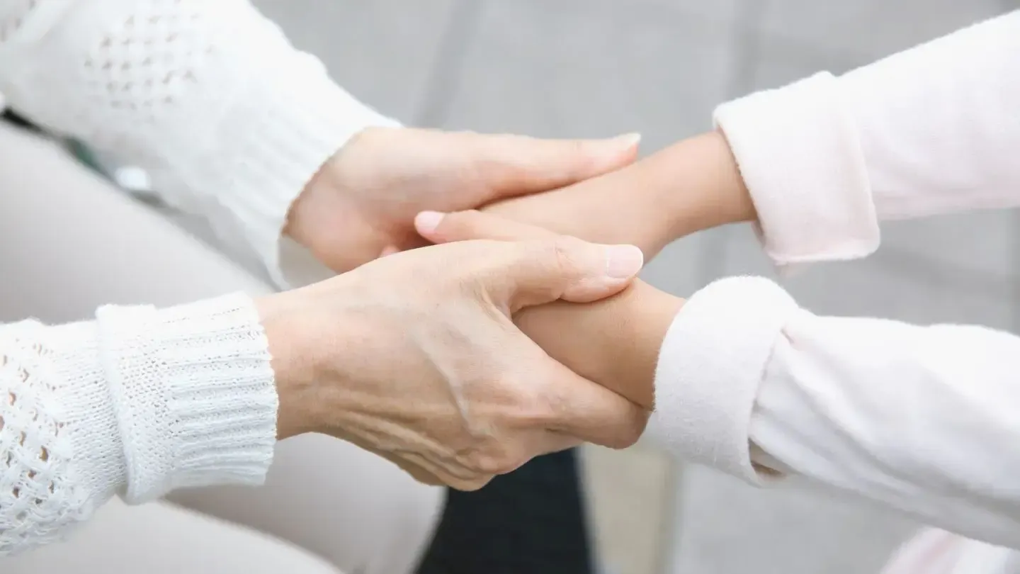 Hands of an adult and child, clasped together, possibly for support or comfort.