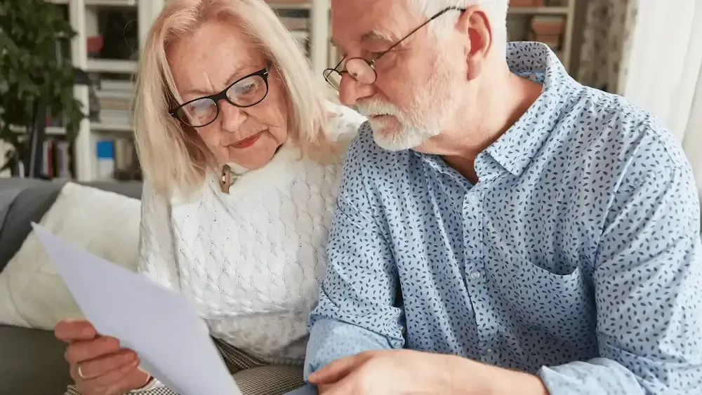 An elderly couple is sitting on a couch looking at a piece of paper.