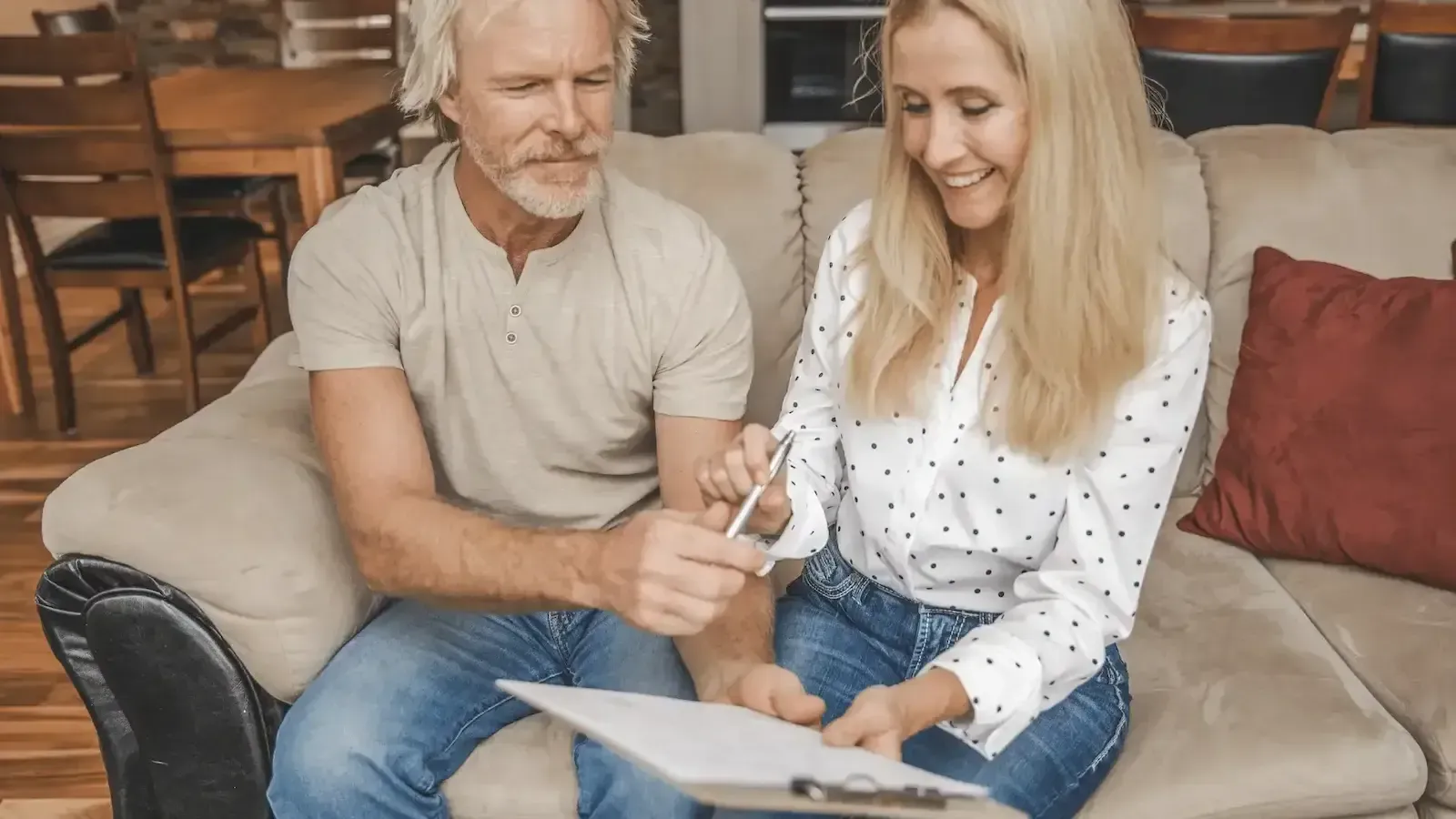 A man and a woman are sitting on a couch looking at a clipboard.