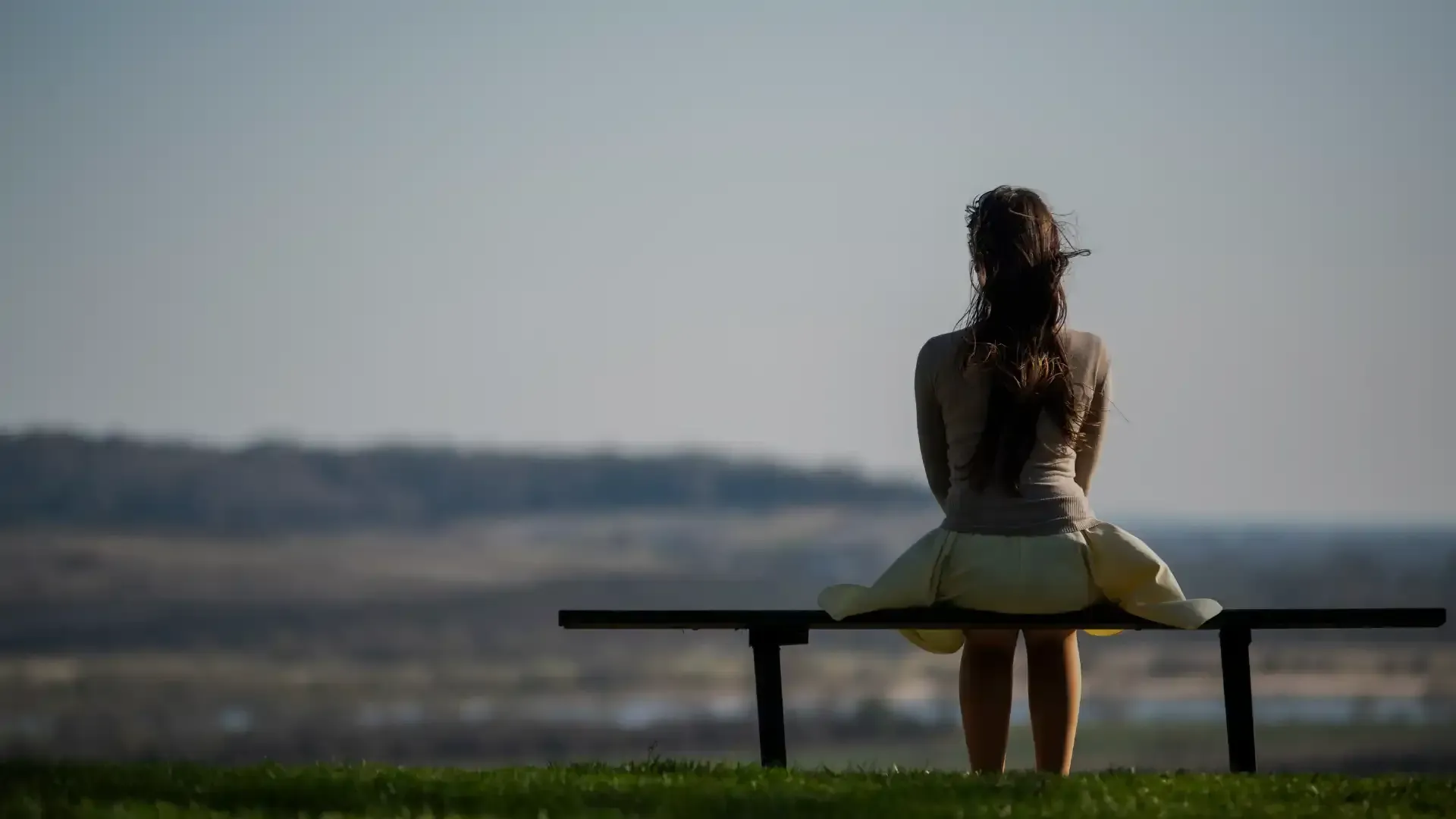 A woman is sitting on a bench looking at the landscape.